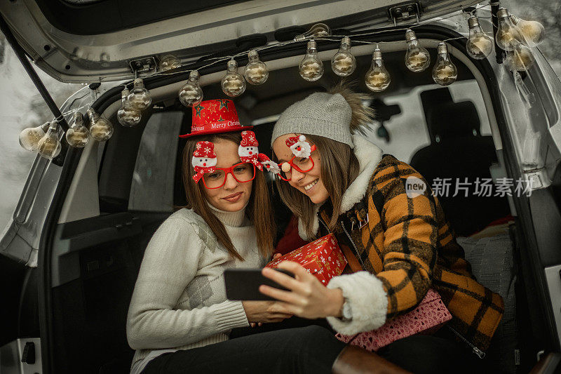 Two women in nature celebrate the new year - Two women in nature celebrate the new year - Two young women celebrate the new year by giving gifts, playing guitar and laugh out - Happy people .两个年轻女性在她们的车里庆祝新年，她们送礼物，弹吉他，放声大笑